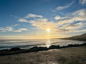 a beach with the sun rising over the ocean at Beyond The Waters Edge Chalet in Dooagh