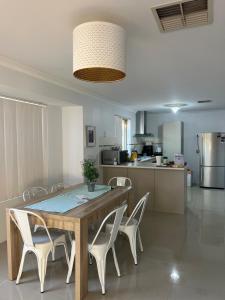 a dining room table with white chairs and a kitchen at Homy Kwinana in Wellard