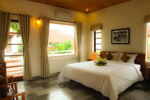 1 dormitorio con 1 cama blanca y 2 ventanas en Charming Homestay, en Hoi An