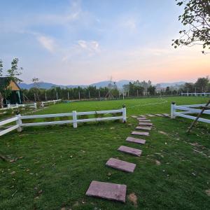 a field with a white fence and stepping stones at ลึกลับรีสอร์ทบ้านนา in Nakhon Nayok