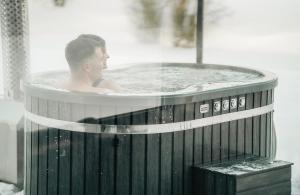 a man sitting in a hot tub in aysicalysicalysicalysicalysicalysicalysical at Privatus romantiškas namelis dviems prie vandens Šilalės rajone in Dirkintai