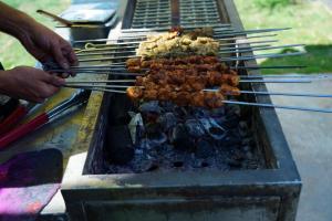 a person cooking food on a grill with tongs at Unwind Farm Retreat in Hyderabad