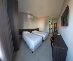 a bedroom with two beds and a table and a television at Vila Dumont no Centro de Foz in Foz do Iguaçu