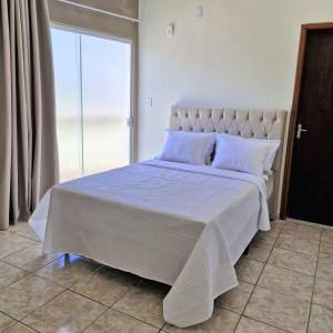 a bedroom with a large white bed with a window at Refúgio Aura,casa com suíte, wi-fi, garagem e churrasqueira in Aparecida