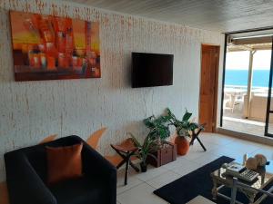 a living room with a couch and a television on a wall at Reñaca - Primera linea de playa con gran terraza in Viña del Mar