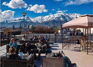 people sitting on a deck with mountains in the background at Guanako Rooftop Hostel in Santiago