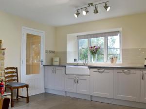 a kitchen with white cabinets and a sink and a window at The Mill Cottage in Ault Hucknall