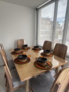 a wooden table with chairs and bowls on it at Siga Sumercé Apartamento completo centro de Duitama in Duitama