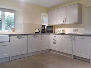 a white kitchen with white cabinets and a window at The Mill Cottage in Ault Hucknall