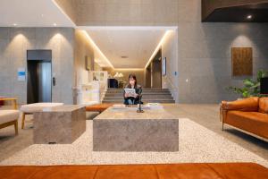 a woman sitting on a chair in a lobby at 부산 엘스테이 호텔 레지던스 EL STAY Busan Long Stay Hotel Residence l 아르떼20 OFF짚라인30 OFF스릴10 OFF 할인 in Busan