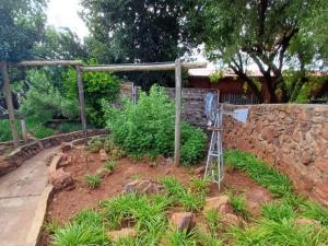 a garden with a stone wall and a ladder at At Ease Road Lodge in Zeerust