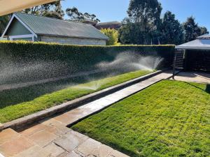 a garden with a hose watering a lawn at Alvane Cottage in Goulburn