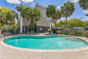 a swimming pool with palm trees and a building at La Quinta by Wyndham Miami Lakes in Miami Lakes