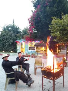 two men sitting in chairs next to a fire at Hotel Rhino Land-Sauraha Family Home in Sauraha