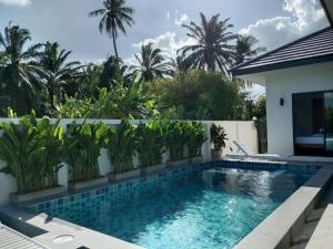 a swimming pool in front of a white fence with palm trees at Niramit Pool Villa in Ban Chong Phli