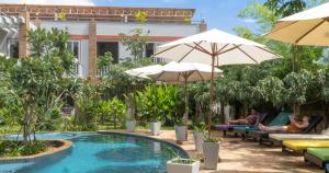 une piscine avec des parasols et 2 personnes assises sur des bancs à côté d'un hôtel dans l'établissement Hak Boutique Hotel, à Siem Reap
