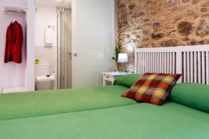 a bedroom with a green bed and a stone wall at Pensión Rua Nova in Santiago de Compostela