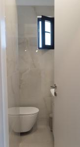 a white bathroom with a toilet and a window at Signature city loft in Tríkala