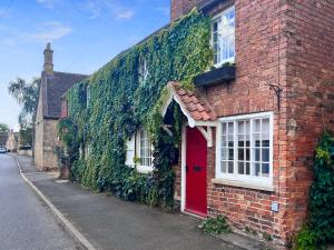 an ivy covered brick house with a red door at Teddy's Cottage in Market Overton