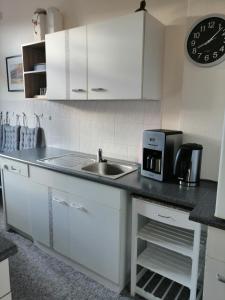 a kitchen with white cabinets and a sink and a clock at Ferienwohnung HARZgeNUSS in Wernigerode