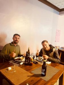 two men sitting at a table with food and beer at CAR-NET HOTEL in Kisoro