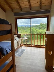 a bedroom with a bed and a balcony with a large window at Cabaña Caburgua vista al Volcán, Senderos del Bosque in Pucón