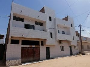 a white building with black doors on a street at Résidence hibis chez M&B in Saly Portudal