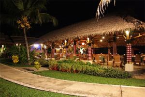 un restaurant avec un toit de paille, des tables et des chaises dans l'établissement Kalicaa Villa Resort, Tanjung Lesung, à Tanjung Lesung