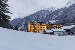 a building in the snow with mountains in the background at Hotel Kirchenwirt in Kaunertal