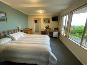 a bedroom with a bed and a desk and windows at Citrus Grove in Nelson