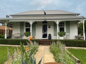 a white house with a porch and a garden at Korumburra Farmhouse in Korumburra
