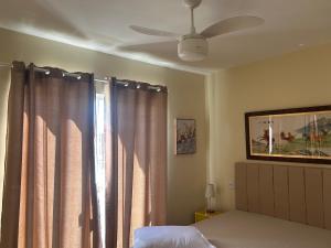 a bedroom with a ceiling fan and a window with curtains at chalé vista para montanha in Penedo