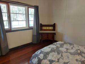 a bedroom with a bed and a table and windows at Forest Edge Cottage Dwellingup in Dwellingup