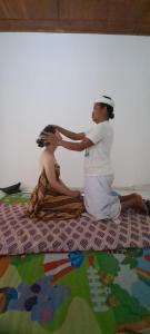 a man and woman sitting on a bed getting their hair at Serongga guest house in Lebih