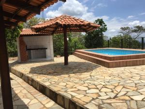 a swimming pool with an umbrella and an outdoor fireplace at Pousada Recanto das Pedras São Leopoldo in Pirenópolis