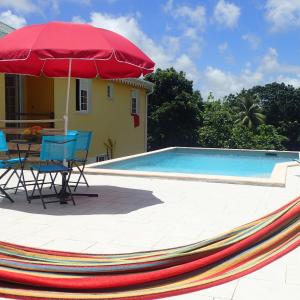 a pool with a table and chairs and a red umbrella at La créola BAYALOCATION in Rivière-Pilote