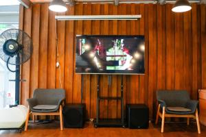 a tv on a wall with three chairs and a fan at Patra Dumai Hotel in Dumai