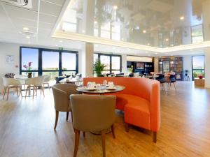 a restaurant with an orange couch and tables and chairs at Kyriad Prestige Residence & Spa Cabourg-Dives-sur-Mer in Dives-sur-Mer