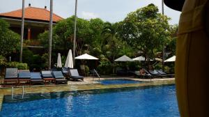 a pool with chairs and umbrellas next to a resort at Swastika Bungalows in Sanur