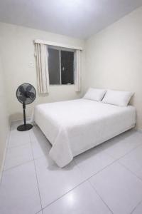a white bedroom with a bed and a fan at Aconchego na praia in Ilhéus