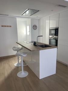 a white kitchen with a sink and two bar stools at Moderno APARTAMENTO CÉNTRICO EN MARBELLA in Marbella +2 photos