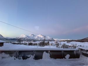 a building covered in snow with mountains in the background at Big cabin in Lyngen Fjords in Jægervatnet