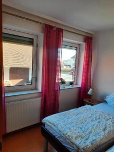 a bedroom with a bed and two windows with red curtains at Ferienwohnung Albus in Albertshausen