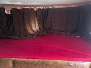 a bed with red sheets and a brown curtain at Autocaravana in Port Saplaya