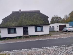 a white house with a grass roof with a car at Fewo Helga in Glowe