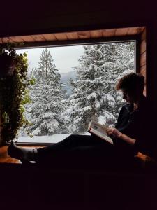 a woman sitting in a window reading a book at Шале над скелею in Krivorovnya