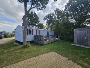 a white tiny house with a porch and a tree at Chalet First Stage - Renesse in Renesse