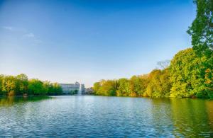 a river with trees and a building in the background at Leonardo Royal Hotel Köln - Am Stadtwald in Cologne