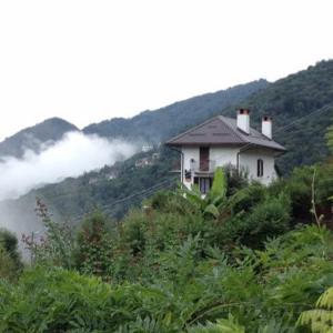 a house on the side of a mountain with clouds at B&B La Locanda del Cinghiale in Aurano