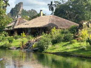 a house with a thatched roof next to a river at THANYAWANA Glamping Tents in Khao Sok National Park